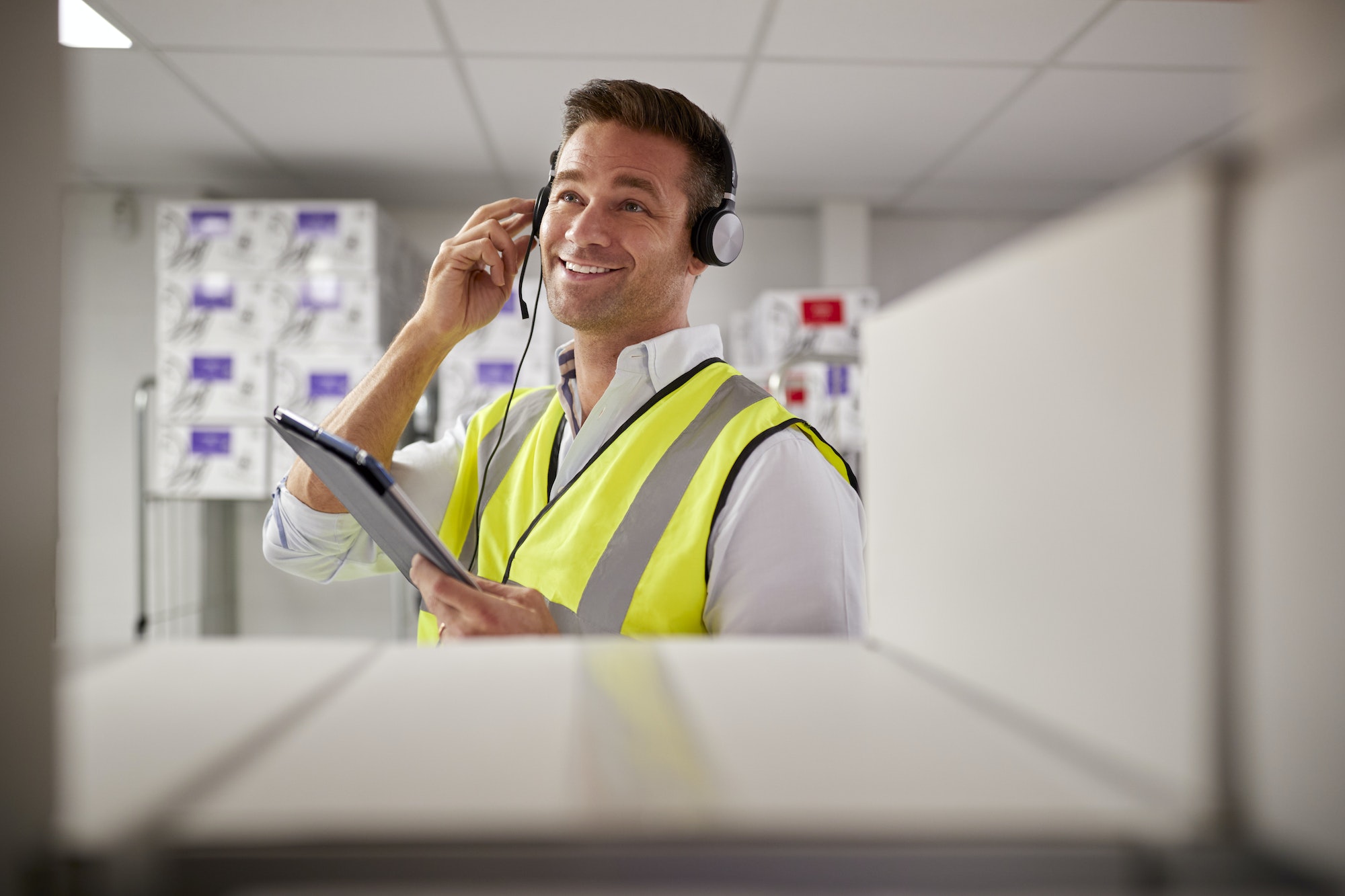 Male Worker Wearing Headset In Logistics Distribution Warehouse With Digital Tablet